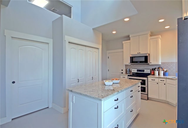 kitchen featuring backsplash, white cabinets, appliances with stainless steel finishes, a kitchen island, and light stone counters