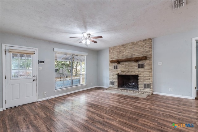 unfurnished living room with dark wood-type flooring, a fireplace, a textured ceiling, and plenty of natural light