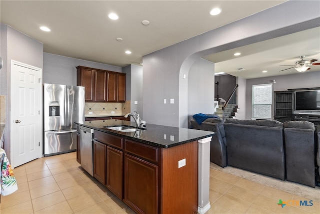 kitchen with stainless steel appliances, decorative backsplash, a kitchen island with sink, dark stone countertops, and sink