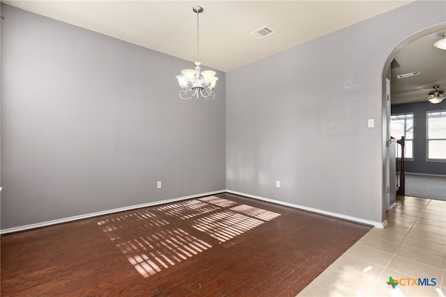 tiled spare room with ceiling fan with notable chandelier