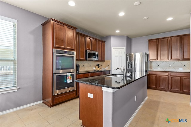 kitchen with decorative backsplash, sink, stainless steel appliances, and a center island with sink