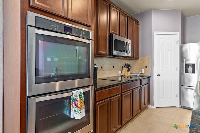 kitchen with light tile patterned floors, decorative backsplash, appliances with stainless steel finishes, and dark stone countertops