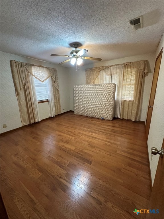 empty room featuring hardwood / wood-style floors, a wealth of natural light, ceiling fan, and a textured ceiling