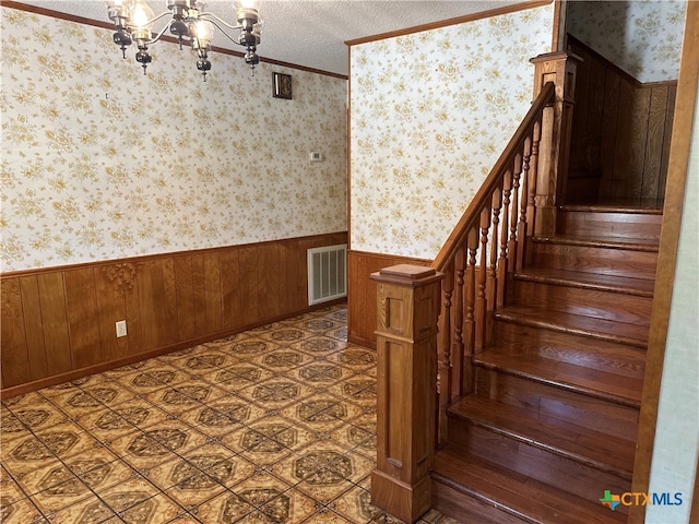 staircase featuring crown molding, wood walls, a textured ceiling, and a chandelier