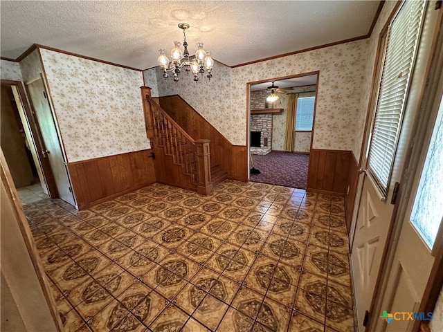 unfurnished dining area with wooden walls, a textured ceiling, ornamental molding, and ceiling fan with notable chandelier