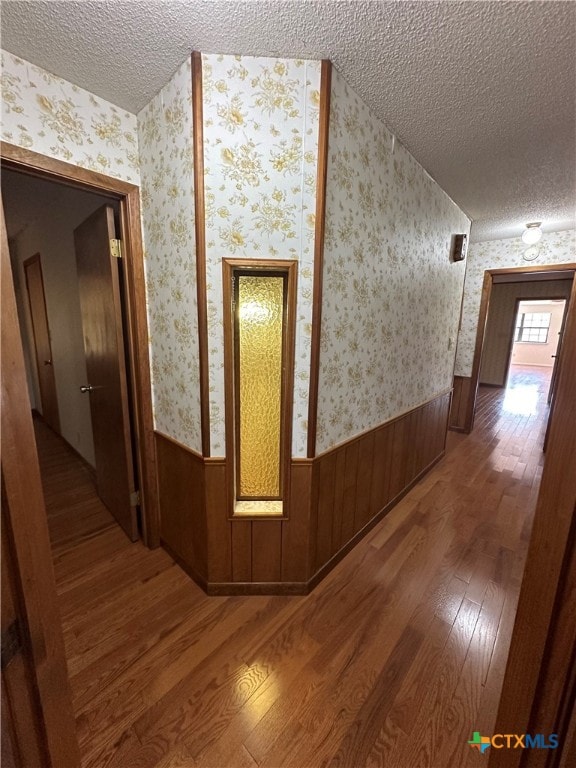 hall featuring wooden walls, a textured ceiling, and hardwood / wood-style flooring