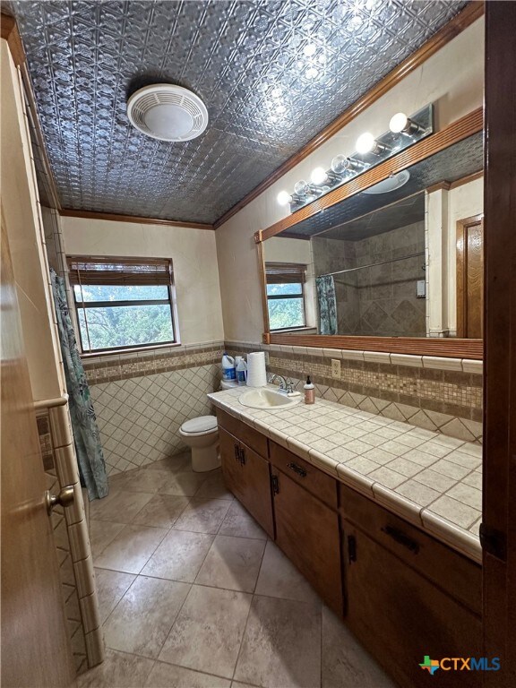 bathroom featuring tile patterned floors, toilet, tile walls, ornamental molding, and vanity