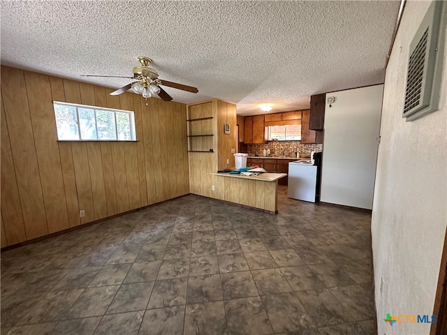 kitchen featuring kitchen peninsula, wood walls, a textured ceiling, tasteful backsplash, and ceiling fan