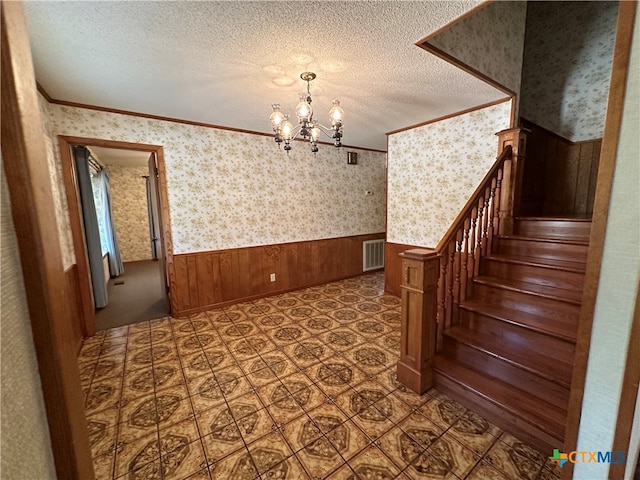 interior space with wood walls, a textured ceiling, a notable chandelier, and crown molding