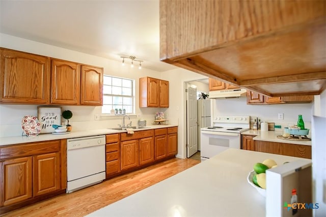 kitchen with white appliances, under cabinet range hood, brown cabinetry, and a sink