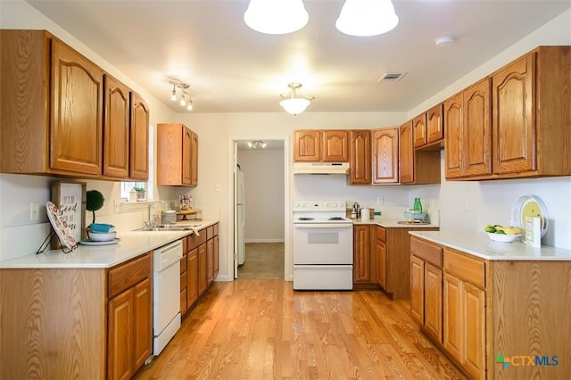 kitchen featuring white appliances, brown cabinets, a sink, and under cabinet range hood