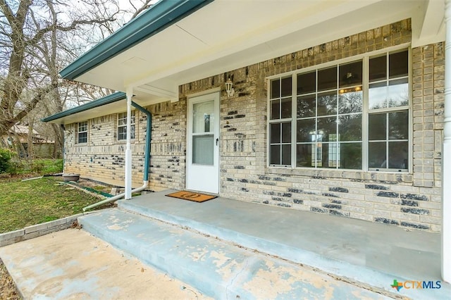 view of exterior entry featuring a porch and brick siding