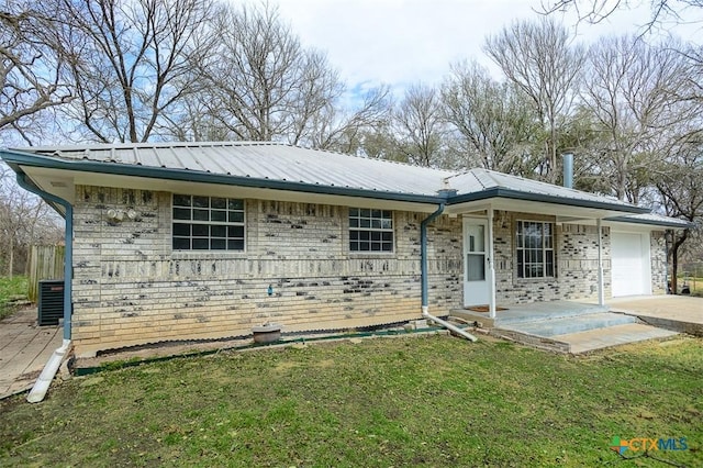 single story home featuring metal roof, an attached garage, central air condition unit, brick siding, and a front yard