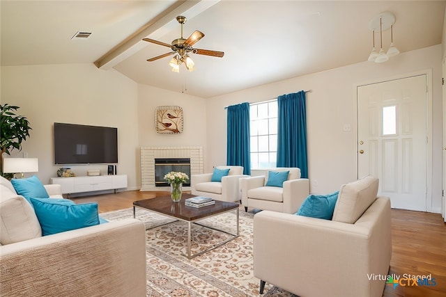 living room featuring a fireplace, visible vents, lofted ceiling with beams, light wood-style floors, and ceiling fan