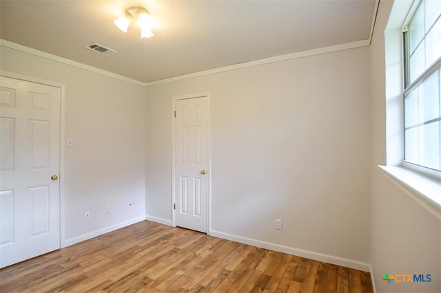 unfurnished room featuring ornamental molding, a wealth of natural light, light wood-style flooring, and visible vents