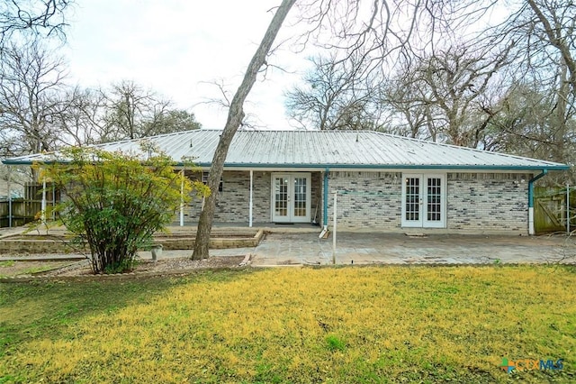 rear view of house with brick siding, metal roof, a lawn, and french doors