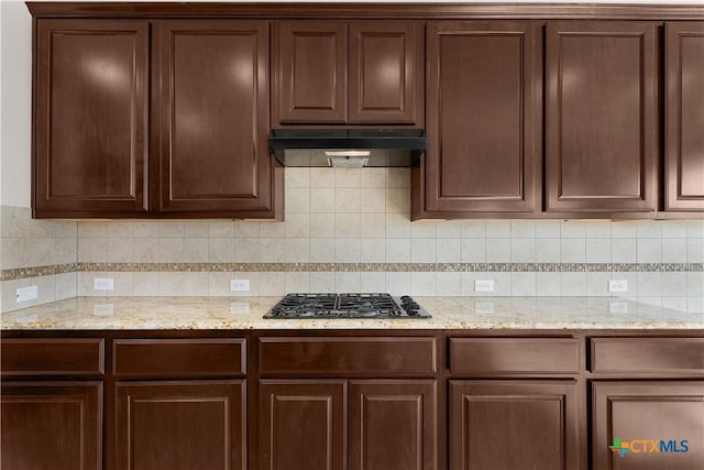 kitchen featuring dark brown cabinets, tasteful backsplash, under cabinet range hood, and gas cooktop