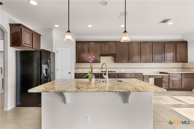 kitchen featuring black refrigerator with ice dispenser, a breakfast bar, visible vents, and light tile patterned floors
