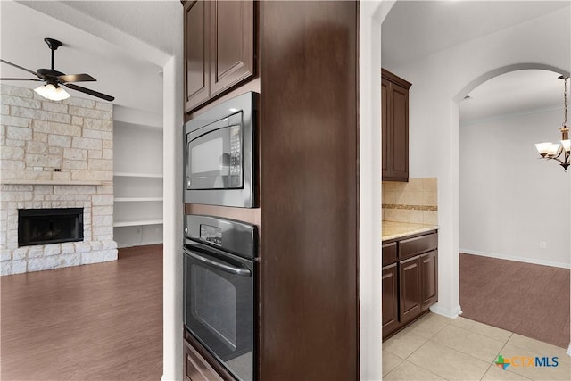 kitchen featuring built in microwave, ceiling fan with notable chandelier, arched walkways, dark brown cabinetry, and black oven