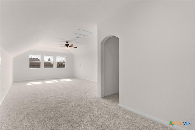 carpeted empty room with vaulted ceiling, baseboards, arched walkways, and a ceiling fan