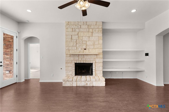 unfurnished living room featuring dark wood finished floors, a ceiling fan, arched walkways, baseboards, and a fireplace