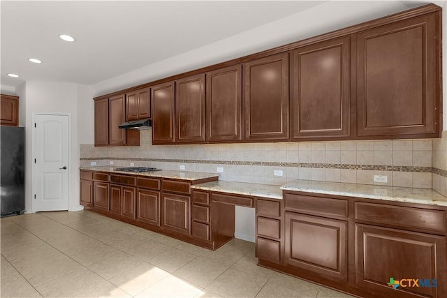 kitchen featuring gas cooktop, under cabinet range hood, tasteful backsplash, and black fridge