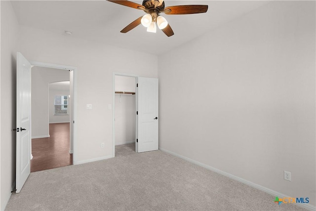 unfurnished bedroom featuring light carpet, arched walkways, baseboards, a ceiling fan, and a closet