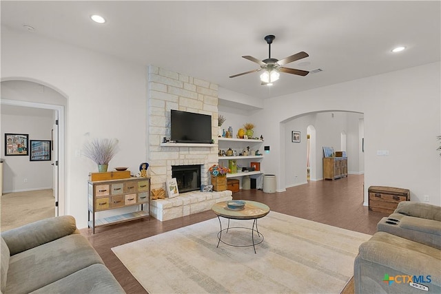 living room with dark wood-type flooring, ceiling fan, and a stone fireplace