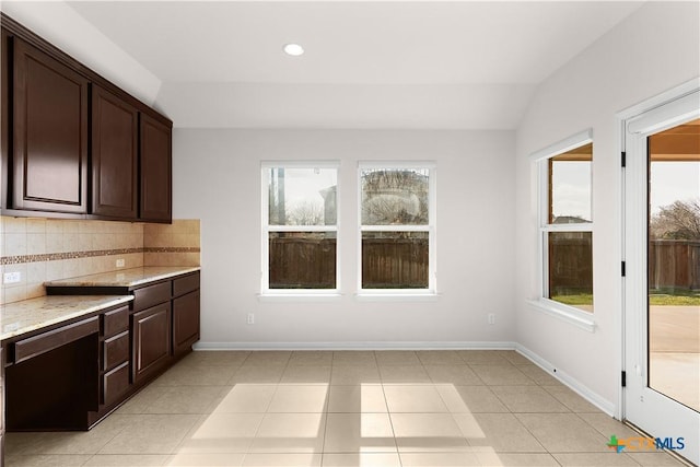 kitchen featuring dark brown cabinets, vaulted ceiling, light stone countertops, and backsplash