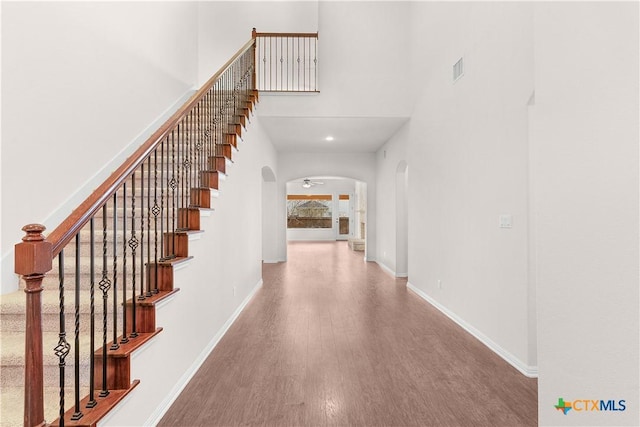 staircase with wood finished floors, arched walkways, baseboards, a high ceiling, and visible vents