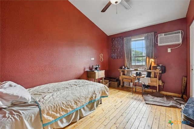 bedroom with ceiling fan, light hardwood / wood-style floors, an AC wall unit, and vaulted ceiling