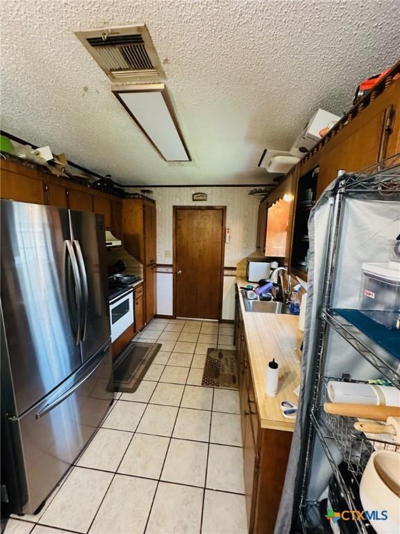 218 Monterrey Dr, Victoria, TX 77904 - kitchen with freestanding refrigerator, a sink, a textured ceiling, wooden counters, and light tile patterned floors