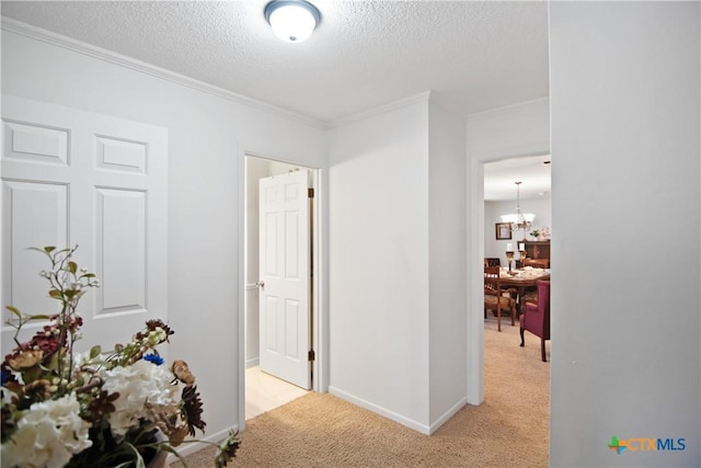 hall with a textured ceiling, crown molding, light carpet, and an inviting chandelier