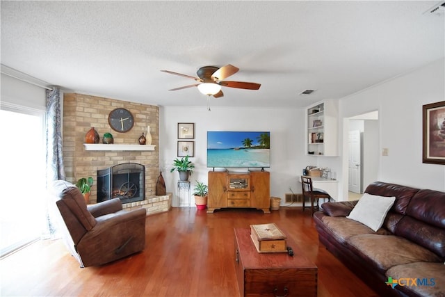 living room featuring a fireplace, wood-type flooring, a textured ceiling, and ceiling fan