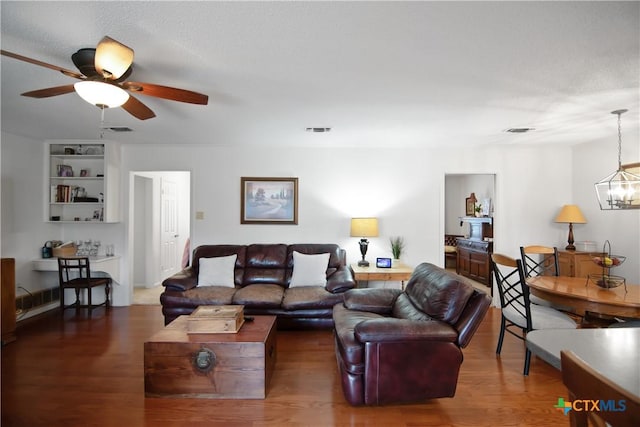 living room with ceiling fan with notable chandelier, a textured ceiling, and dark hardwood / wood-style flooring