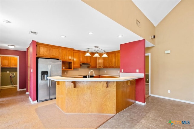 kitchen featuring stainless steel refrigerator with ice dispenser, a breakfast bar, sink, kitchen peninsula, and pendant lighting