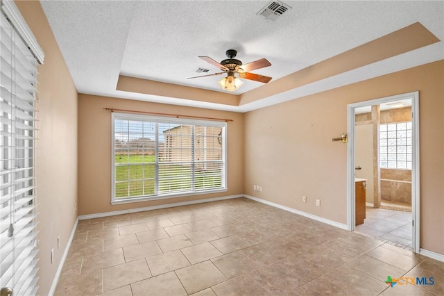 spare room featuring light tile patterned floors, a wealth of natural light, a textured ceiling, and a tray ceiling