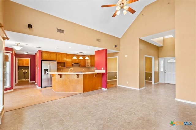 kitchen with stainless steel refrigerator with ice dispenser, a breakfast bar area, high vaulted ceiling, kitchen peninsula, and ceiling fan