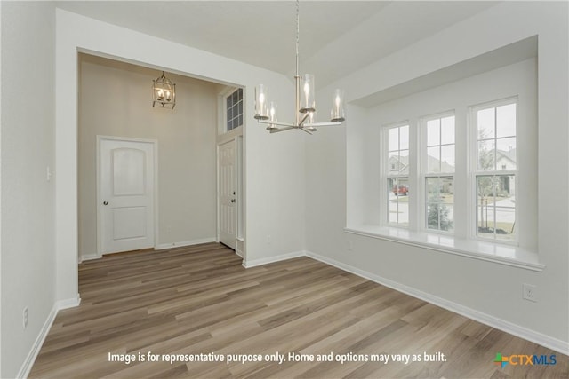 unfurnished dining area with baseboards, an inviting chandelier, and wood finished floors