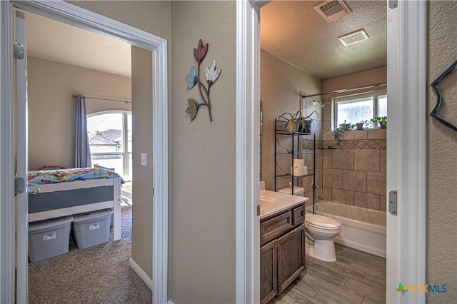 full bathroom with tiled shower / bath combo, wood-type flooring, a textured ceiling, toilet, and vanity