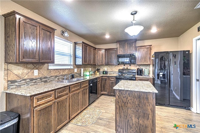 kitchen featuring light stone countertops, sink, black appliances, light hardwood / wood-style floors, and a kitchen island