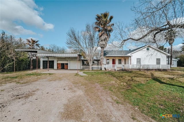 ranch-style house featuring a front lawn, a porch, dirt driveway, a garage, and a carport