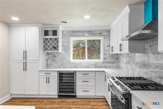 111 Warwick Glen St, Victoria, TX 77904 - kitchen with beverage cooler, stainless steel range with gas cooktop, wall chimney range hood, light countertops, and white cabinetry
