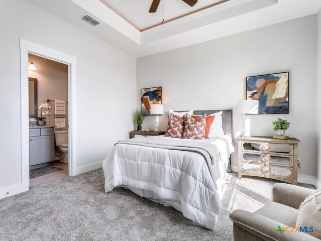 carpeted bedroom featuring a tray ceiling, ensuite bath, and ceiling fan