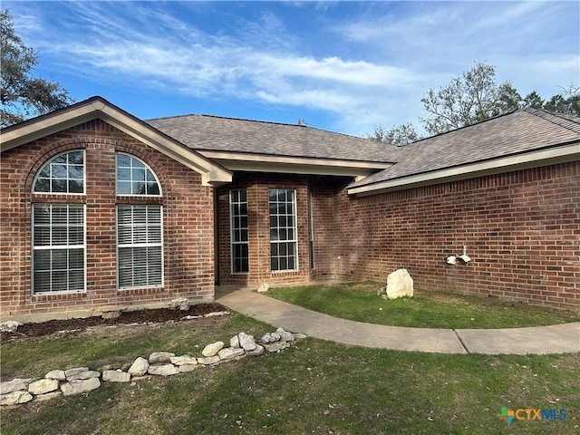 view of front facade with brick siding and a shingled roof