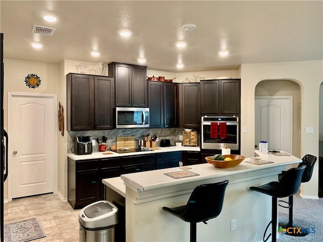 kitchen featuring a breakfast bar area, light countertops, appliances with stainless steel finishes, dark brown cabinetry, and an island with sink