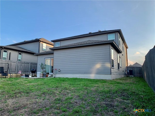 back of house at dusk with a lawn and a fenced backyard