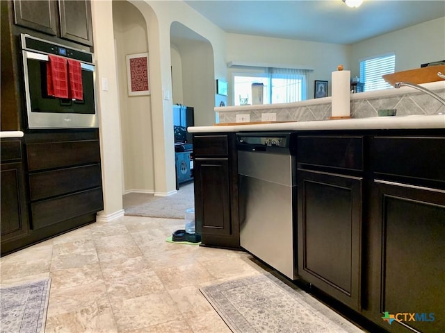 kitchen with arched walkways, stainless steel appliances, light countertops, decorative backsplash, and dark brown cabinets