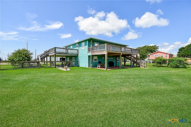 rear view of property featuring a lawn, a wooden deck, and a patio