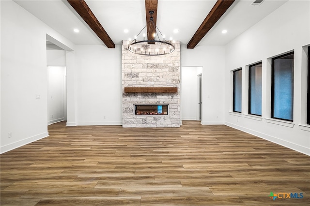 unfurnished living room featuring a stone fireplace, an inviting chandelier, beamed ceiling, and wood-type flooring